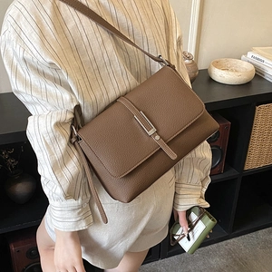 Detail showing the pebbled leather texture and silver buckle of the brown crossbody bag