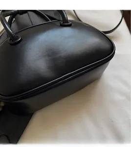 Close-up of the smooth black leather texture and rounded handle of the bowling handbag