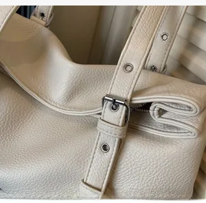 Detail of adjustable shoulder strap with silver metal buckle on beige leather tote bag