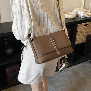 Brown leather crossbody bag with flap and metal buckle shown in a lifestyle street setting