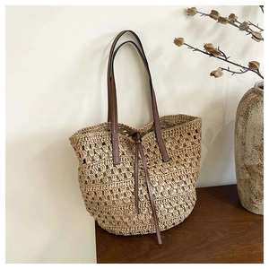 Detail of hand-woven straw tote bag with brown leather handles on wooden surface