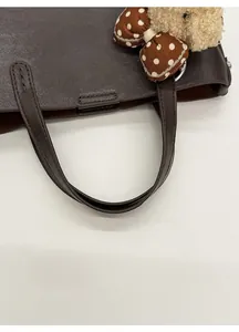 Détail de la poignée en cuir rembourrée et du charm ours en peluche marron du sac