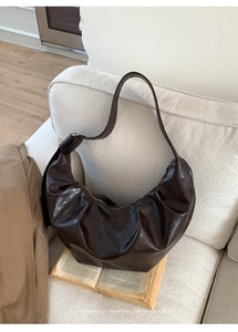 Détail d'un sac demi-lune en cuir plissé marron foncé posé sur un canapé blanc chic