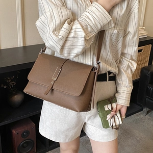 Detail shot of a brown crossbody bag with lychee texture and silver metal buckle