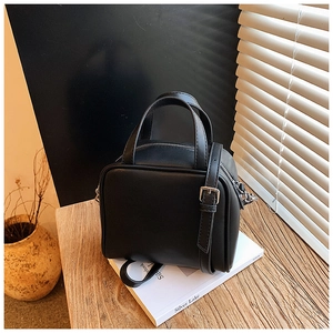 Detailed close-up of a black leather handbag with silver zippers on a wooden table setup