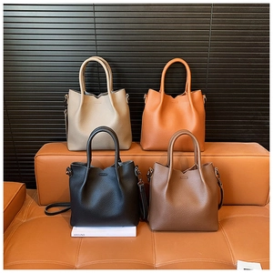 Litchi pattern leather tote bags in four colors shown on a stylish brown leather bench