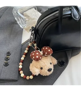 Detail of cute teddy dog plush charm with polka dot bow and beaded chain on a bag