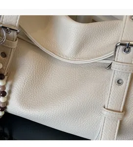 Detailed view of cream leather shoulder bag texture with beaded lanyard and buckle