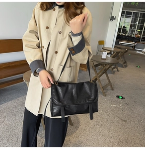 Close-up of black textured leather flap bag with decorative vertical straps and shoulder strap