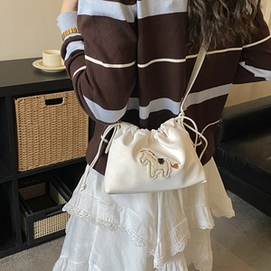 Detail view of the white drawstring bucket bag with horse embroidery on model
