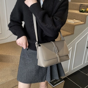 Chic taupe textured leather crossbody bag styled with a minimalist outfit on wooden stairs