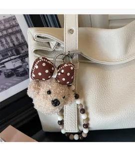 Detail of plush bear charm with polka dot bow and beaded strap on white leather bag