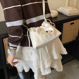 Detail showing the white drawstring bucket bag with horse embroidery and thin leather strap