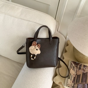 Détail d'un sac seau en similicuir marron foncé avec un charmant ours en peluche attaché