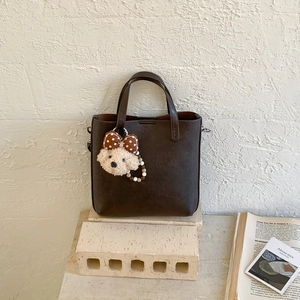Détail du sac seau en cuir marron foncé avec texture litchi et pendentif en peluche