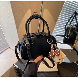 Detail of black bowling handbag with plush puppy charm and adjustable strap held by model