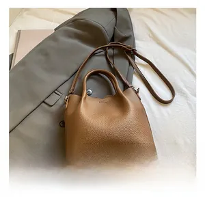 Brown lychee leather bucket bag displayed on white fabric with a stylish grey blazer
