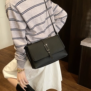 Close-up of black crossbody bag with silver buckle worn by a model in a cozy indoor setting