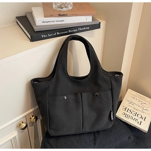 Detailed macro view of black canvas tote bag featuring front pockets and metal button closure