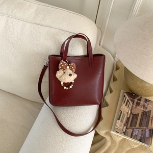Détail d'un sac seau bordeaux avec charm d'ours et perles sur un canapé blanc