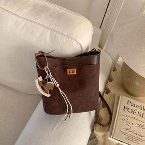 Detail of coffee brown bucket bag with gold lock, tassel and horse charm on white sofa