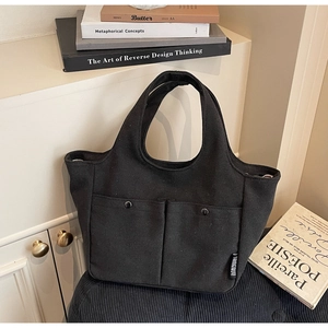 Detail of minimalist black canvas tote bag with metal snap pockets and woven side label