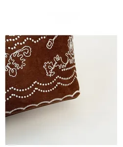 Gros plan d'un sac en daim marron avec broderie florale blanche et texture souple