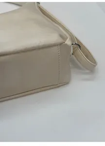 Detail view of the widened bottom structure and metal hardware on a cream leather tote bag