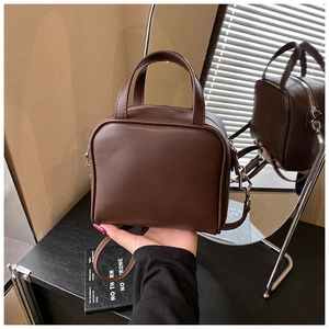 Detail of dark brown leather handbag with dual handles and smooth finish in soft light