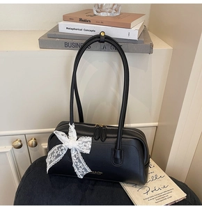 Close-up of black lychee grain leather bag with white lace bow and gold zippers