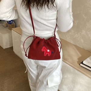 Detail of red drawstring bucket bag featuring a blue horse embroidery and slim strap