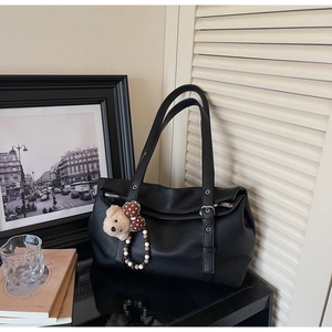Detail of black pebbled leather tote bag with a cute bear charm and adjustable shoulder straps