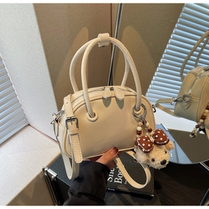 Close-up of cream Boston bag with silver zippers and a brown plush bear charm