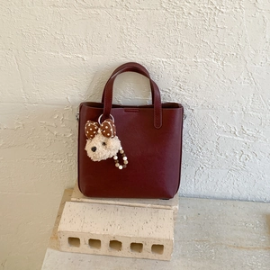 Détail d'un sac seau en cuir bordeaux avec une peluche de chiot et un nœud à pois chic