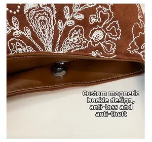 Détail du sac seau en daim marron avec broderies florales blanches et fermoir magnétique