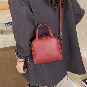 Detail view of a dark red faux leather satchel bag with silver metal hooks and strap