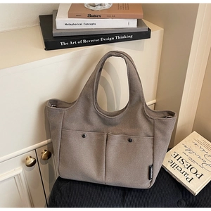 Detail of tan canvas tote bag showing two front pockets with premium metal snap buttons