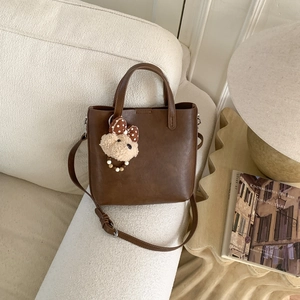 Détail d'un sac seau en cuir marron foncé avec un ours en peluche sur une table en bois