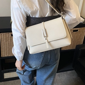 Back view of a white pebble leather crossbody bag worn by a model in a home setting