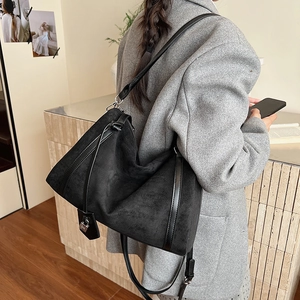 Dettaglio borsa tote grande in camoscio nero con ciondolo a lucchetto su un blazer grigio