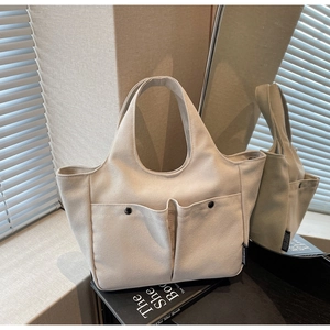Detail of cream canvas tote bag with front pockets and black metal snap buttons