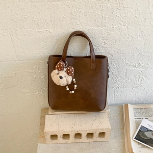 Sac seau en cuir marron avec charm ours en peluche et chaîne perlée sur support en pierre