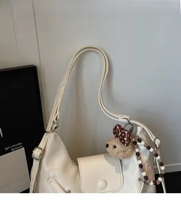 Detail of cream leather hobo bag with teddy bear charm and beaded chain accessory