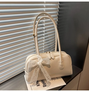 Close-up of cream Boston bag with lychee grain leather and lace bow detail