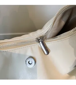 Close-up of white leather handbag showing silver metal zipper and magnetic snap closure