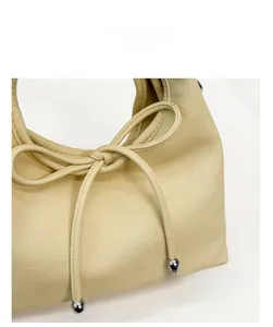 Detailed close-up of beige lychee grain faux leather handbag with elegant bow tie and metal bead