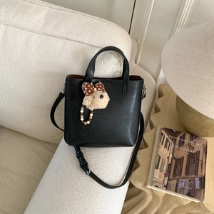 Détail d'un sac seau noir mat avec un pendentif ours en peluche sur un canapé