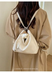 Detail view of a beige leather backpack with tassel zipper and cute plush charm pendant