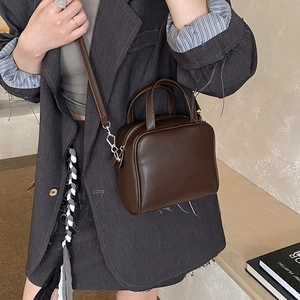 Detail of a dark brown crossbody small square bag with silver metal hardware connectors