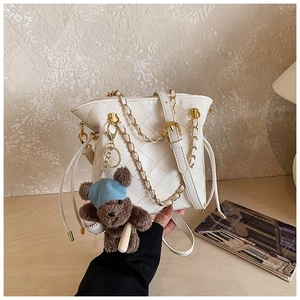 Detail of white quilted bucket bag with gold chain and cute teddy bear charm